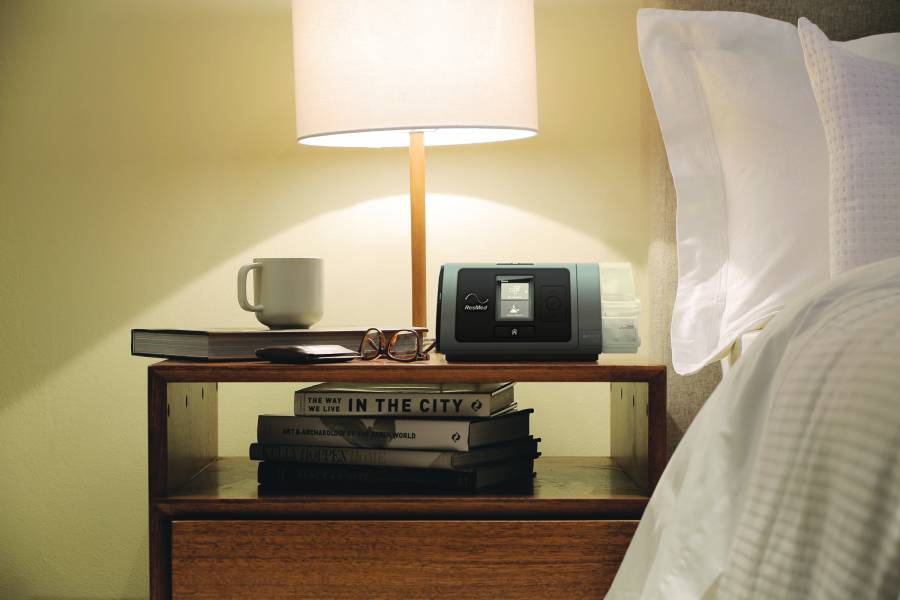 A well-lit examination table sits in the center of the frame. On its surface, a medical machine, possibly for monitoring vitals, is displayed with various dials and readouts. Several medical textbooks, likely open for reference, are stacked beside the machine. A focused light source, perhaps an adjustable examination lamp, illuminates the table and equipment. This image evokes a sense of a doctor's office or examination room, prepared for patient care.